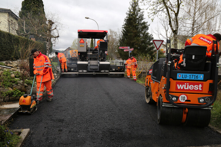Bauarbeiter beim Einbau des Asphaltbelags auf der Güter- und Gemeindestrasse in Alberswil mit einer Belagseinbaumaschine und einer Walze.