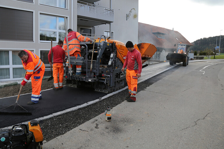 Bauarbeiter beim Einbau des Asphaltbelags auf der Güter- und Gemeindestrasse in Alberswil mit einer Belagseinbaumaschine und einem Radlader.