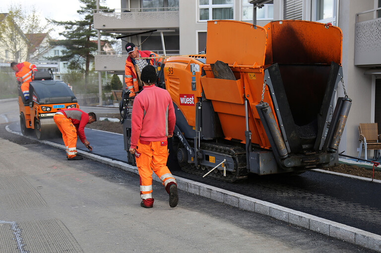 Bauarbeiter beim Einbau des Asphaltbelags auf der Güter- und Gemeindestrasse in Alberswil mit einer Belagseinbaumaschine und einer Walze.